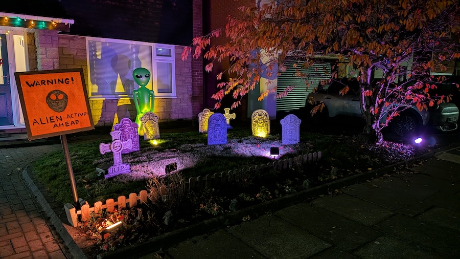 Wide view of the graveyard scene, with illuminated gravestones, an alien in the background and a 'Warning' sign in the foreground.