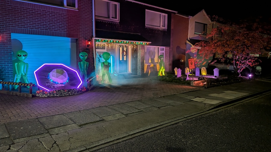 This year's Halloween Scene is an alien invasion. There is a large, crashed UFO surrounded by inflatable aliens. One alien is holding a blaster and has shot a laser beam at a skeleton. There is a graveyard scene, with an autumnal tree containing another crashed UFO.